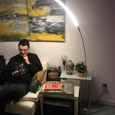 Person on a white couch looking at a phone, floor lamp and abstract art in the background